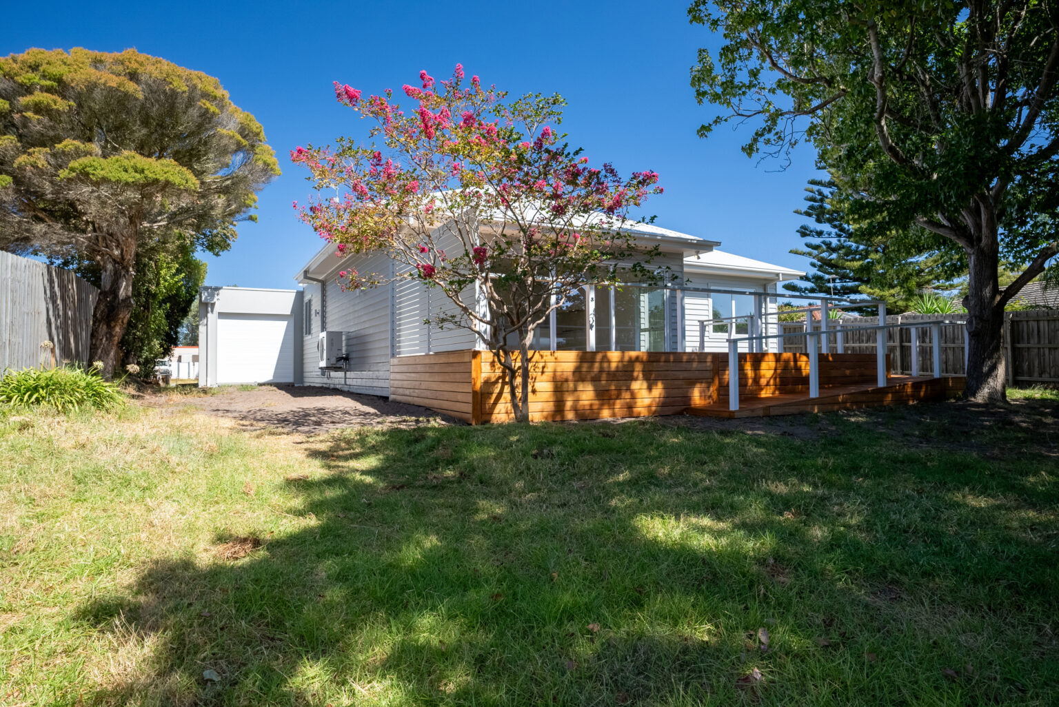 Completed home with grey weatherboard cladding and a timber deck surrounded by established trees