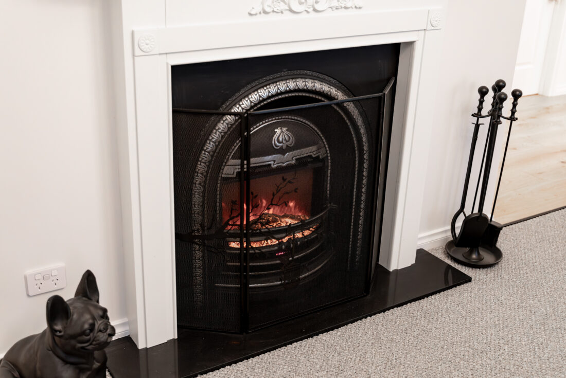 Fireplace with an arched cast iron insert and a white timber mantle